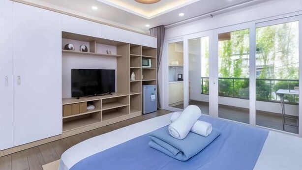 A modern bedroom with a bed, built-in TV, storage cabinets, and a balcony with a view. - Cozrum Homes - Yoga Corner (Ho Chi Minh City)