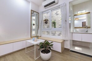 A room with a window, a small table with a potted plant, a white sink, and a mirror. - Cozrum Homes - Yoga Corner (Ho Chi Minh City)