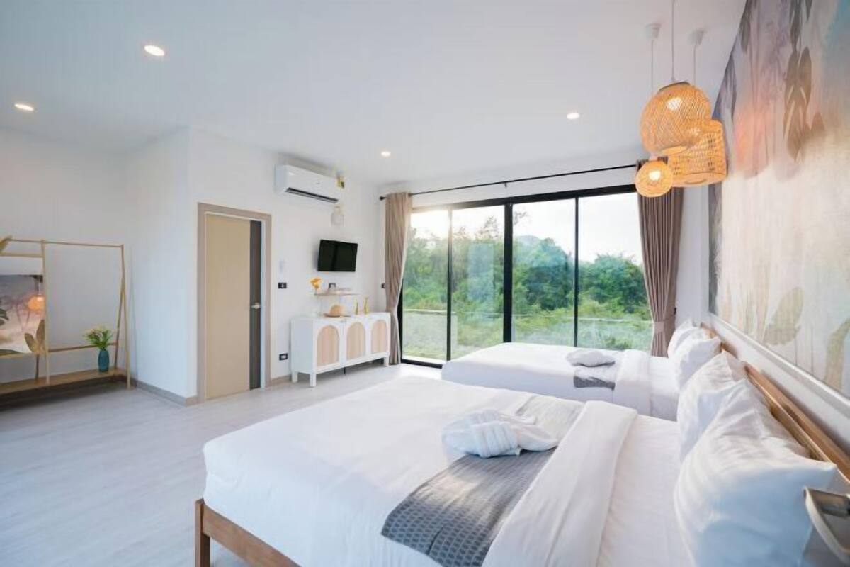 A modern bedroom with a large bed, a dresser, a TV, and a balcony with a view.