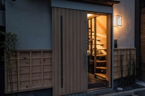 Pared exterior de madera con una puerta corrediza que da a una habitación con una escalera visible.