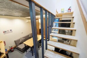 Un escalier avec des marches en bois et une rampe bleue, menant à un palier où se trouvent une table et un canapé.