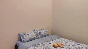 A small bedroom with a bed, two pillows, and a folded towel on the bed.