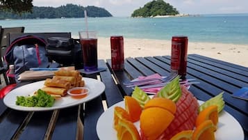 Una mesa con un plato de comida, una bebida y vistas a la playa.