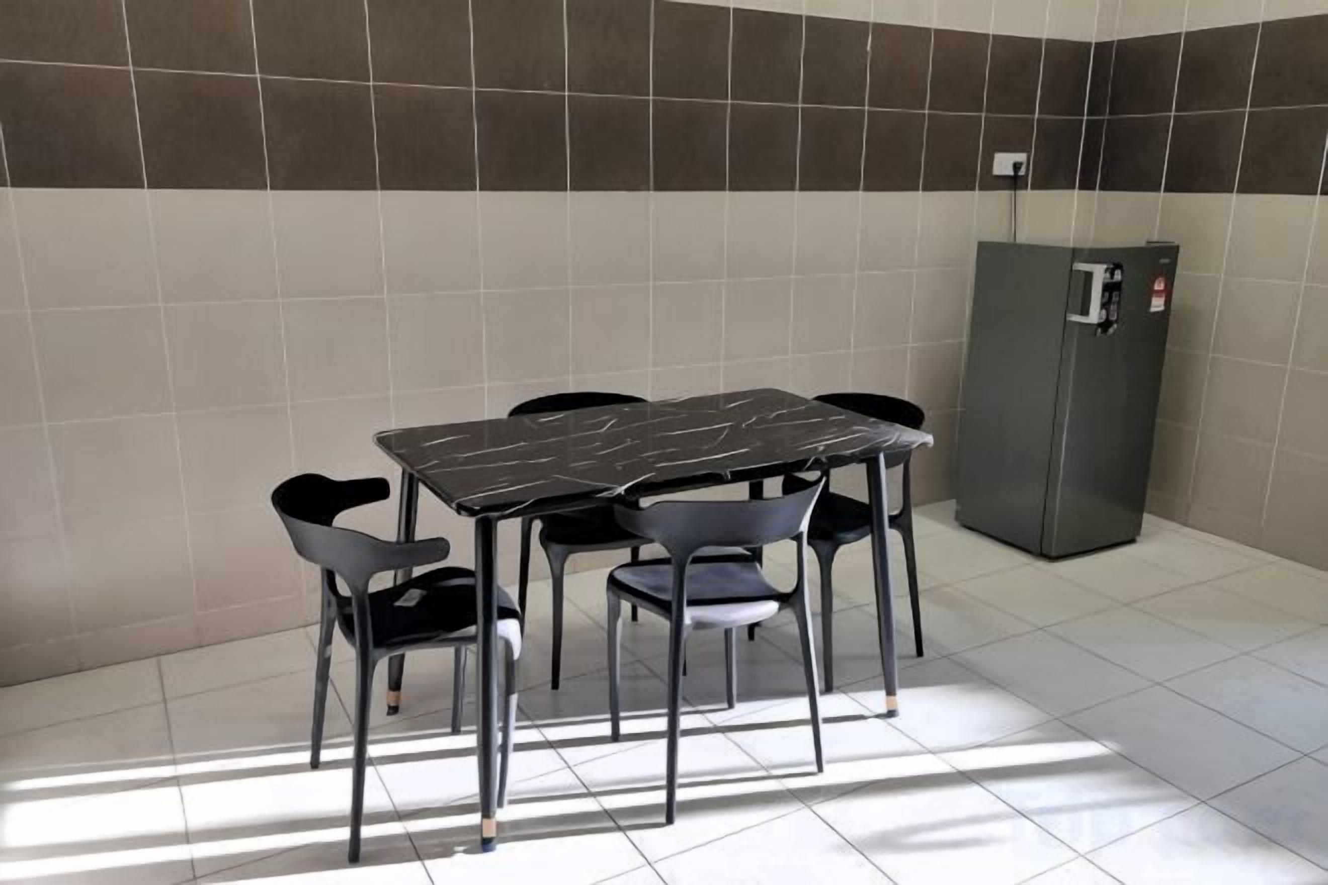 A small dining area with a table and chairs, a refrigerator, and tiled walls.