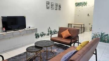 Una sala de estar con sofá, mesa de centro, televisor y plantas decorativas.