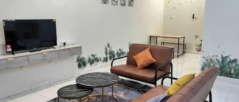 Una sala de estar con sofá, mesa de centro, televisor y plantas decorativas.