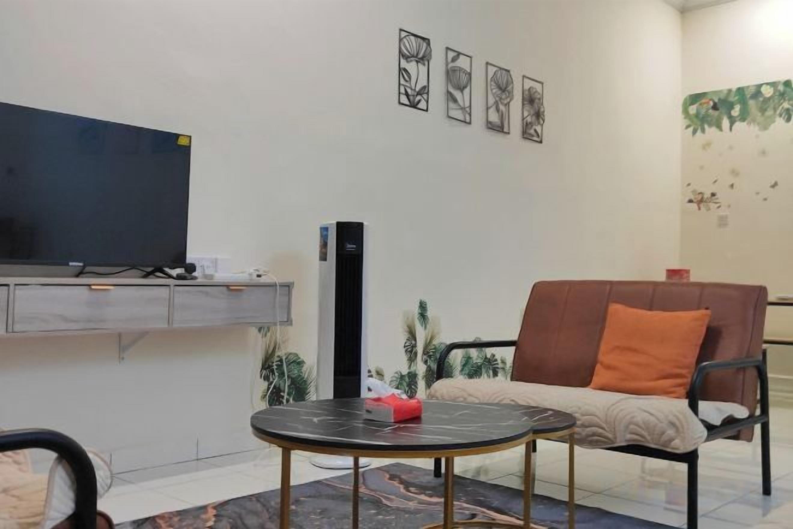 A room with a flat-screen TV, a sofa with an orange cushion, a small round table with a red object, and a wall-mounted cabinet.