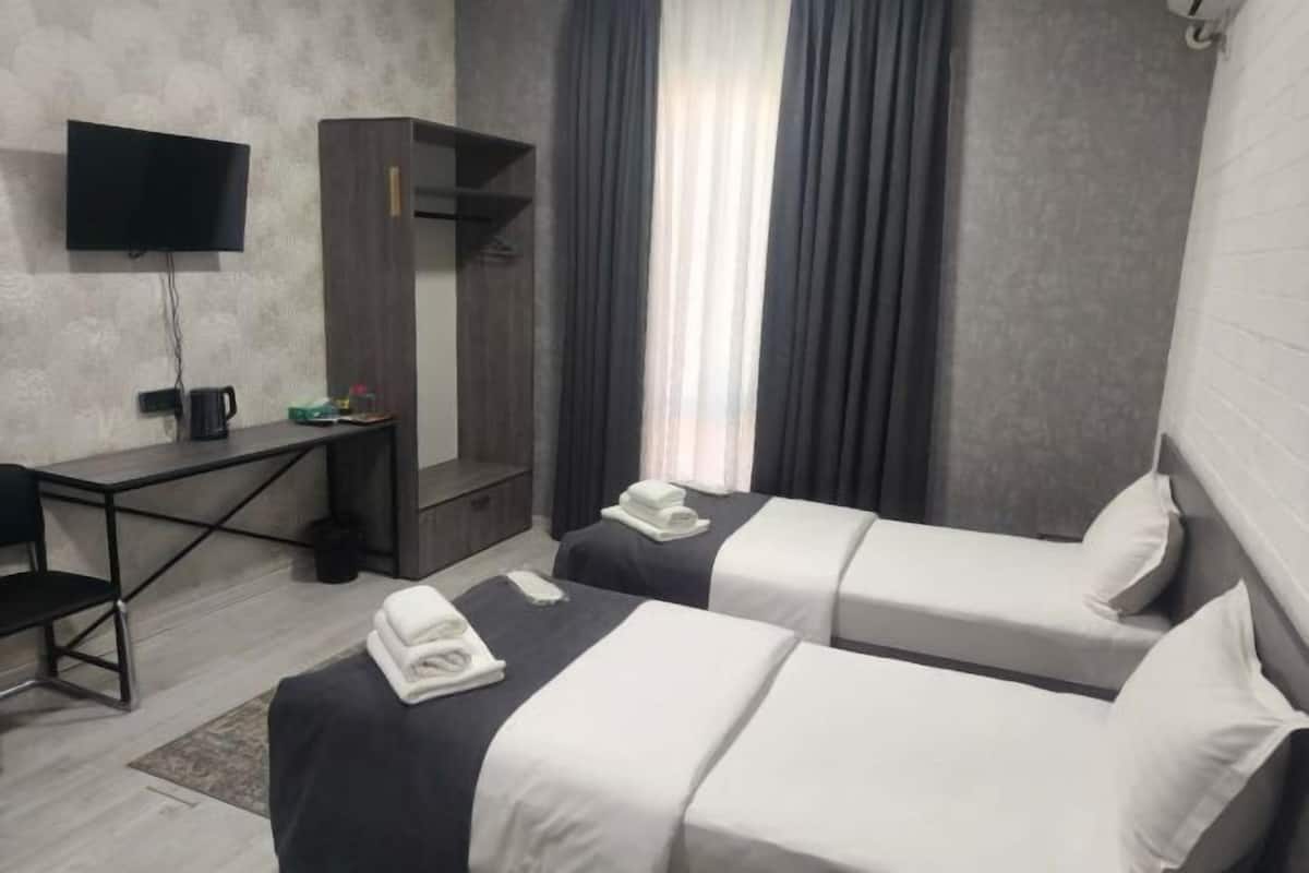 A hotel room with two beds, a desk, a TV, and a window with curtains.