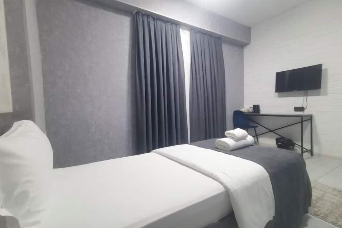 A hotel room with a bed, a desk, a chair, a TV, and a window with curtains.