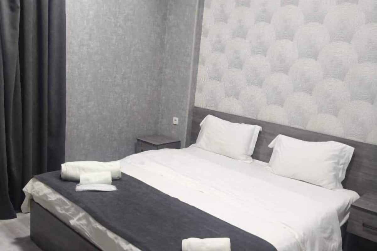 A neatly made bed with white linens, a grey headboard, and a grey patterned wall.