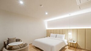 A modern hotel room with a bed, bedside table, lamp, and a round seating area. - Masan Den Basta hotel Gyeongnam Uni (Changwon)