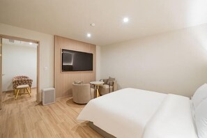 A hotel room with a large bed, a TV mounted on the wall, a small round table with chairs, and a seating area with a cushioned chair. - Masan Den Basta hotel Gyeongnam Uni (Changwon)