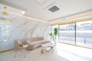 A modern hotel lobby with a marble wall, a beige sofa, a round coffee table, and a large window with a view. - Masan Den Basta hotel Gyeongnam Uni (Changwon)