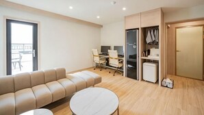 Ein modernes Wohnzimmer mit einer Couch, einem runden Couchtisch, einem Schreibtisch mit Computer und einem Kleiderschrank.
