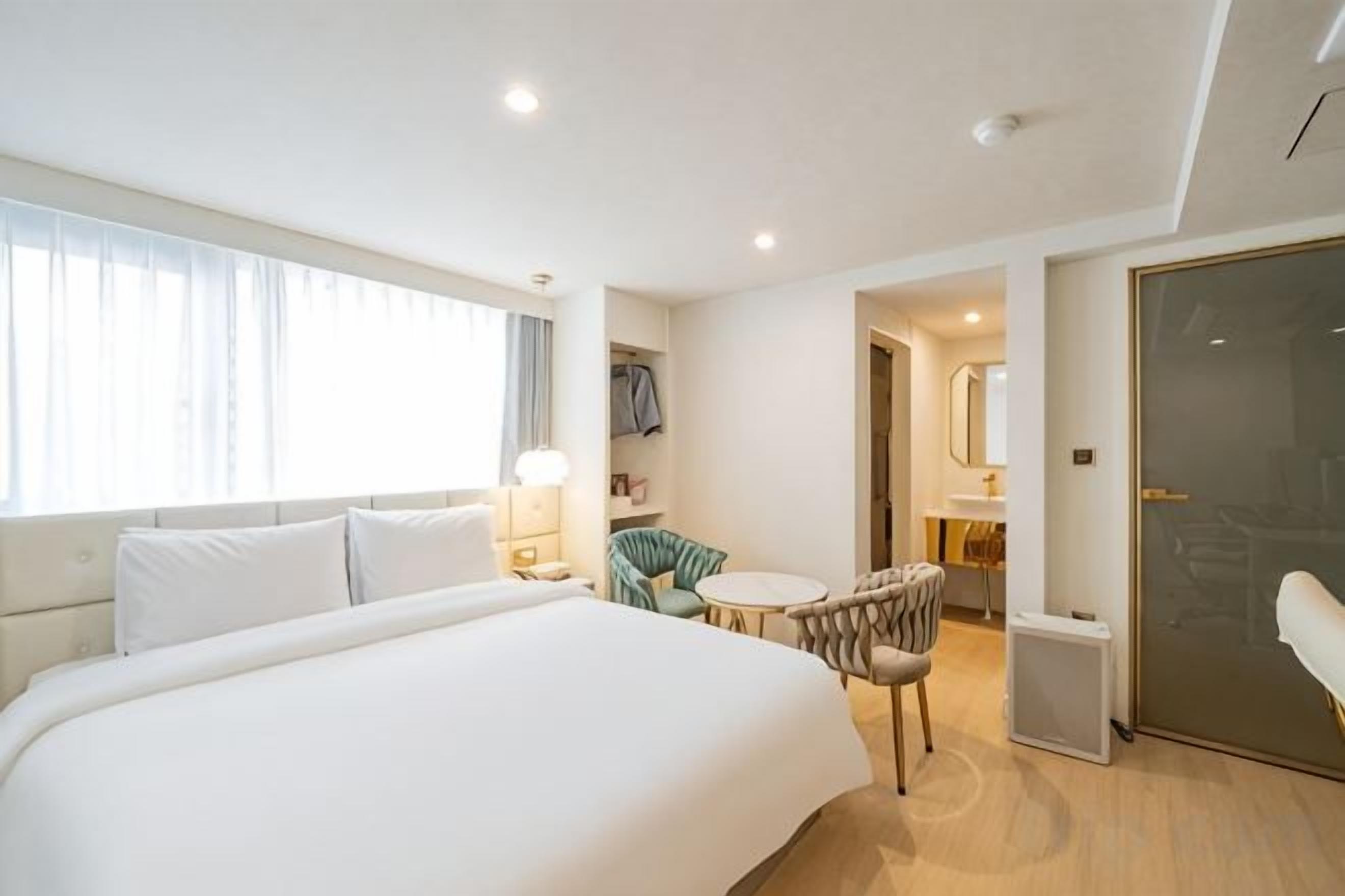 Habitación de hotel con una cama grande, una mesita redonda, una silla, un escritorio y un espejo.