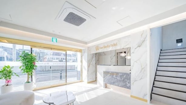 A modern hotel lobby with a reception desk, a staircase, and large windows. - Masan Den Basta hotel Gyeongnam Uni (Changwon)