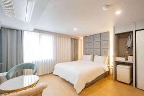 Habitación de hotel con cama, escritorio, silla, armario y ventana con cortinas.