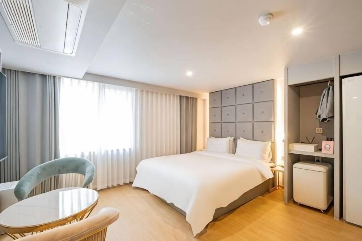 A hotel room with a bed, a chair, a desk, a wardrobe, and a window with curtains.
