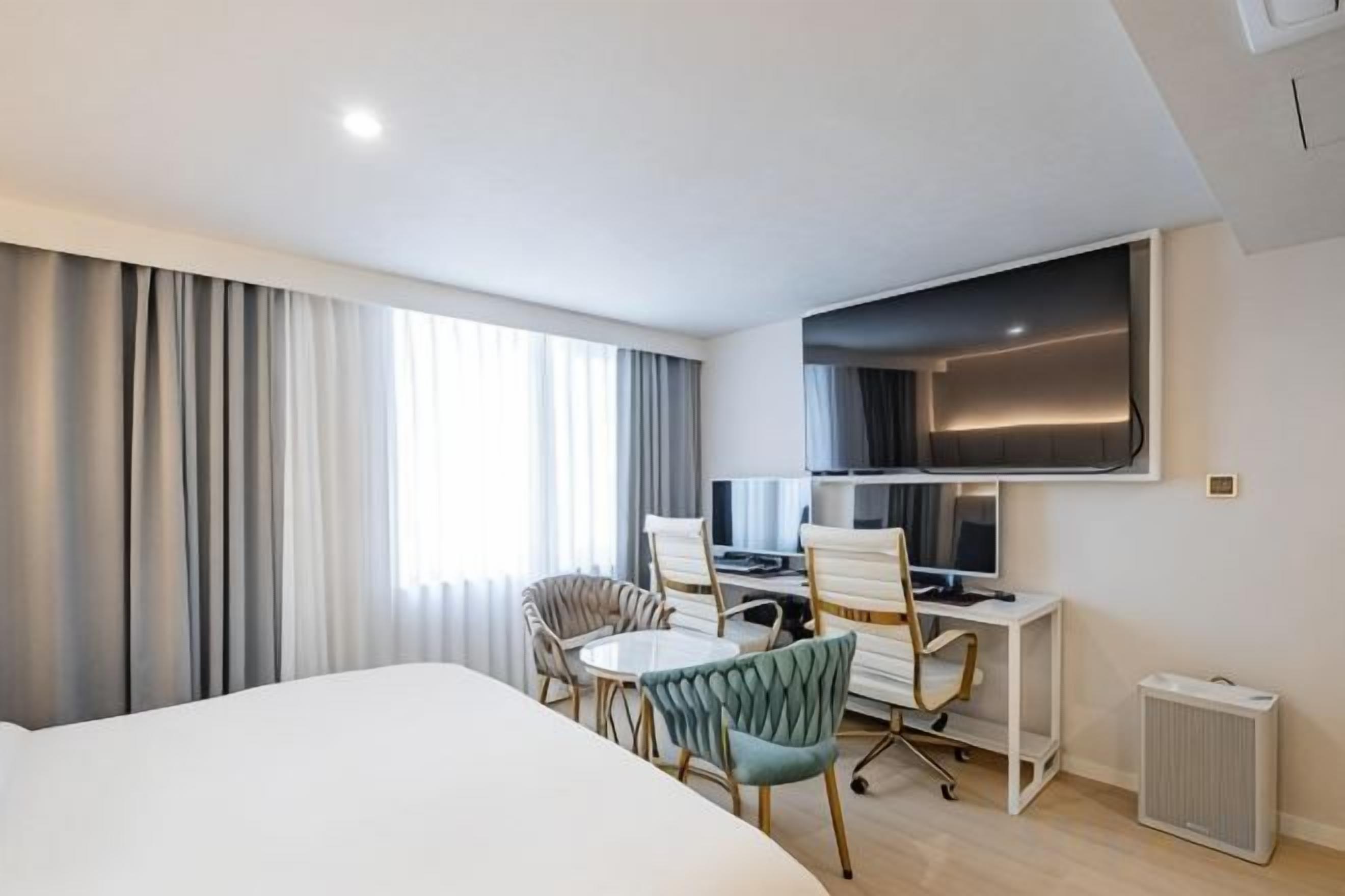 A hotel room with a bed, a desk with a computer, two chairs, and a television.