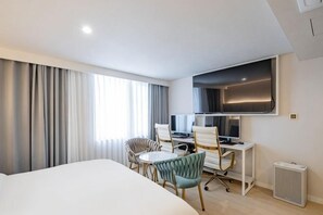 Habitación de hotel con una cama, un escritorio con computadora, dos sillas y un televisor.
