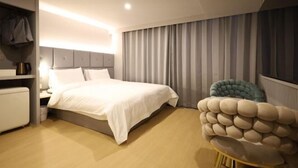 Ein modernes Hotelzimmer mit Bett, Nachttisch, Lampe und einem einzigartigen, runden Sessel.
