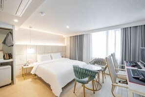 A hotel room with a bed, a desk with a computer, a chair, a small table, and a window with curtains. - Masan Den Basta hotel Gyeongnam Uni (Changwon)