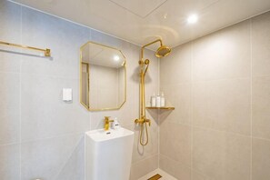A bathroom with a white sink, gold fixtures, a mirror, and a shower. - Masan Den Basta hotel Gyeongnam Uni (Changwon)