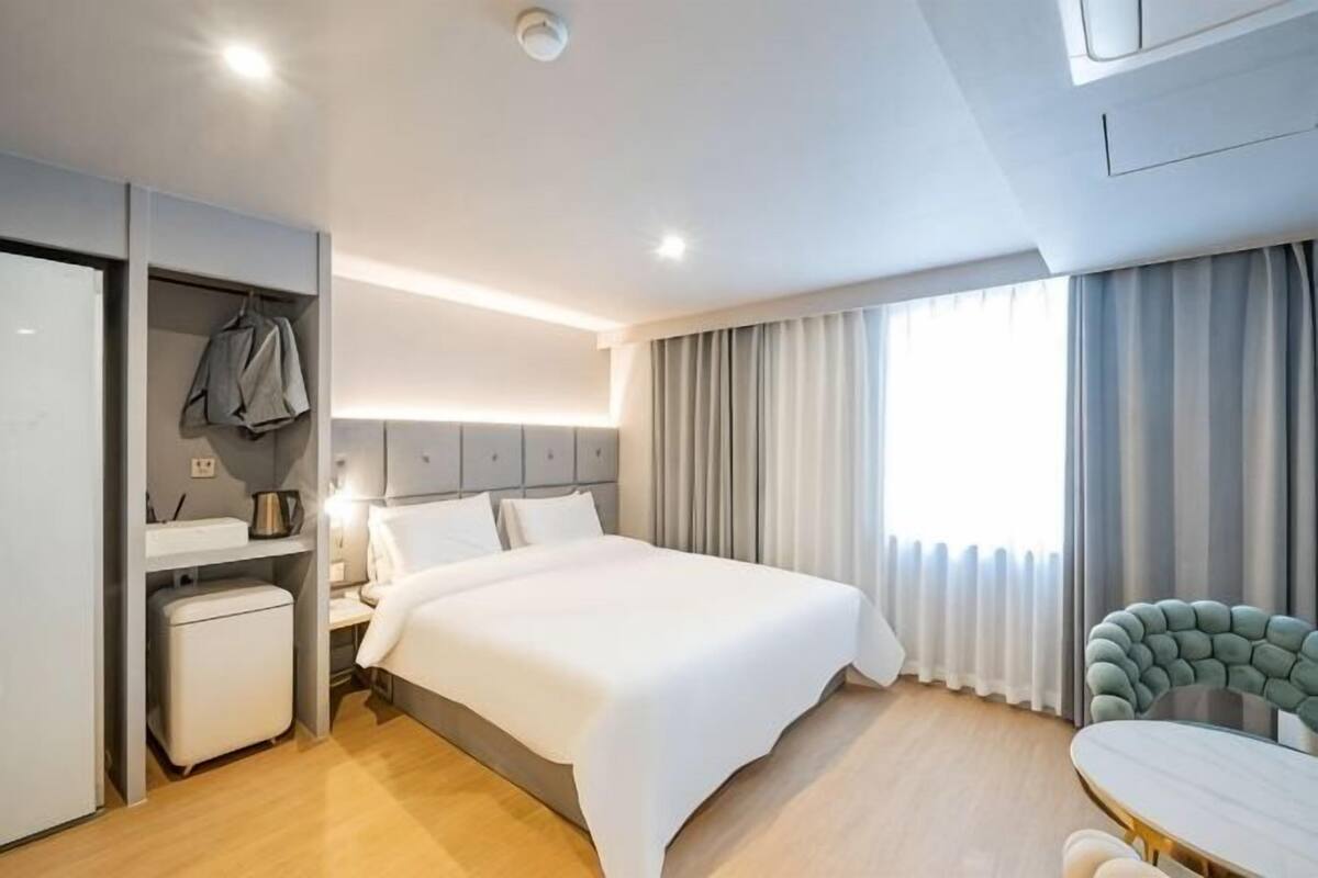 A hotel room with a bed, bedside table, lamp, wardrobe, and a chair.