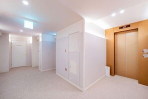 A hallway with white walls, a wooden door, and a light fixture on the ceiling. - Masan Den Basta hotel Gyeongnam Uni (Changwon)