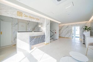 A hotel reception area with a marble reception desk, a staircase, and a modern interior design. - Masan Den Basta hotel Gyeongnam Uni (Changwon)
