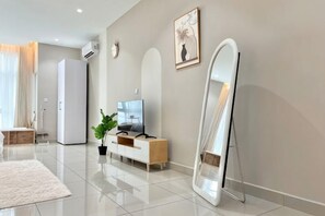 Een moderne woonkamer met een flatscreen televisie, een witte bank, een grote spiegel en een plant in pot.