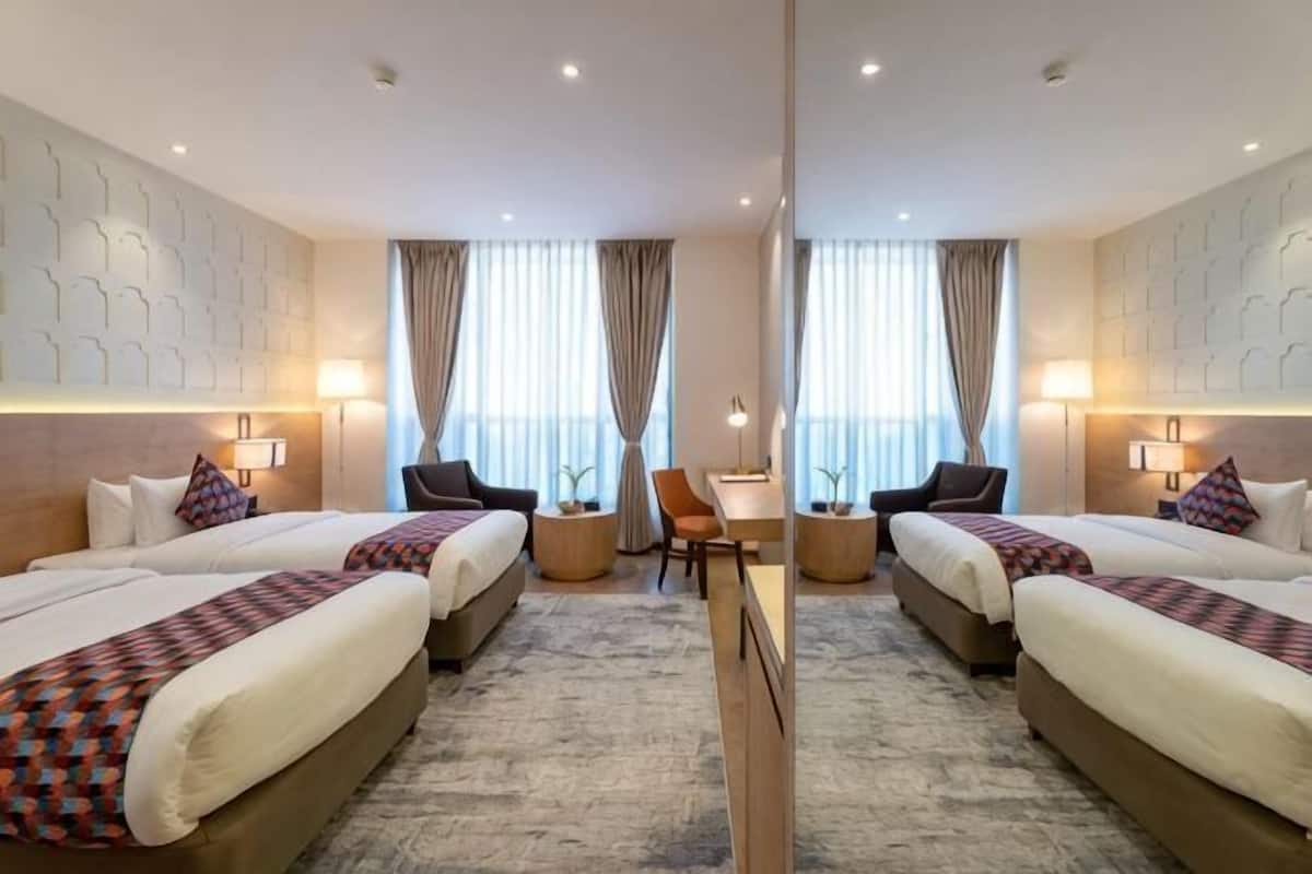 A hotel room with two beds, a desk, and a chair.