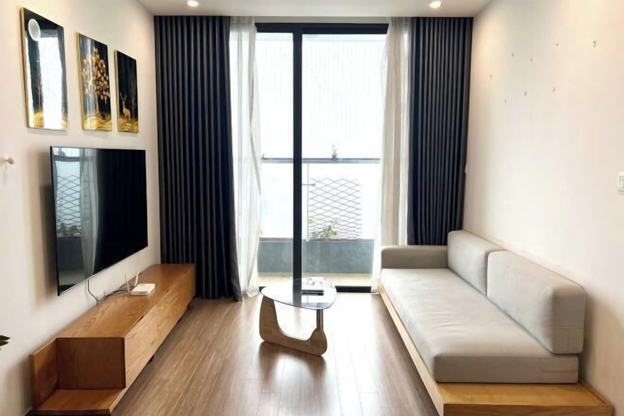En moderne stue med et fladskærms-tv, en sofa, et sofabord og udsigt til en balkon.