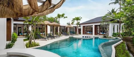 A swimming pool area with lounge chairs, a thatched-roof structure, and a poolside building.