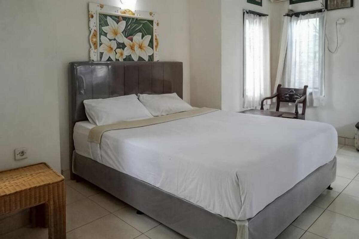 A bed with a headboard, a bedside table, and a chair in a room with white walls and a tiled floor.