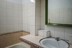 A bathroom with white tiles, a bathtub, a sink, and a mirror with a green frame. - Daton House Near Bali Zoo Ubud Mitra RedDoorz (Bali)