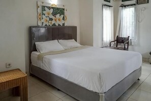 A bed with a headboard, a bedside table, and a chair in a room with white walls and a tiled floor. - Daton House Near Bali Zoo Ubud Mitra RedDoorz (Bali)