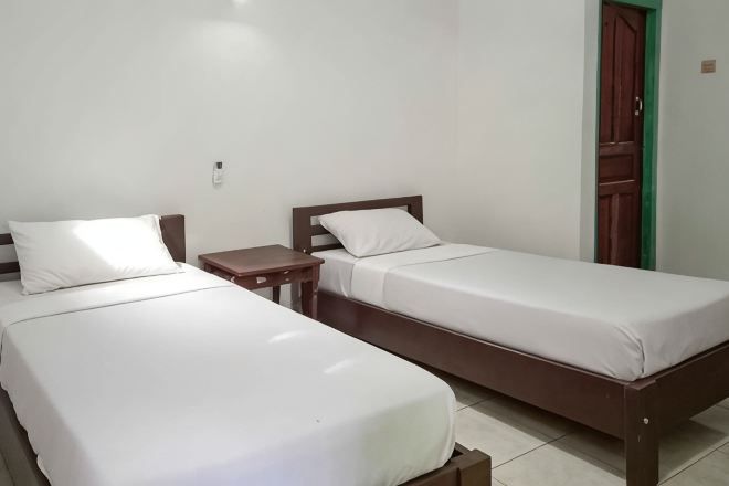 Dos camas individuales con cabeceros de madera y ropa blanca en una habitación con suelo de baldosas y una puerta verde.