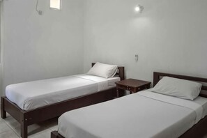 Dos camas individuales con estructura de madera y ropa de cama blanca, una mesita de noche pequeña y una lámpara fijada a la pared.