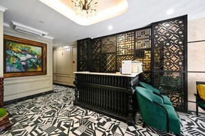 A reception area with a black and white patterned floor, a reception desk, and a green seating area. - Ohana Hotel - Near Bitexco (Ho Chi Minh City)