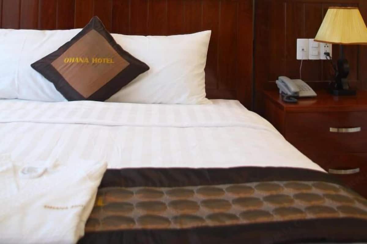 Une chambre d’hôtel avec un lit, un oreiller orné du texte « GHANA HOTEL », une lampe de chevet, un téléphone et une table de chevet.