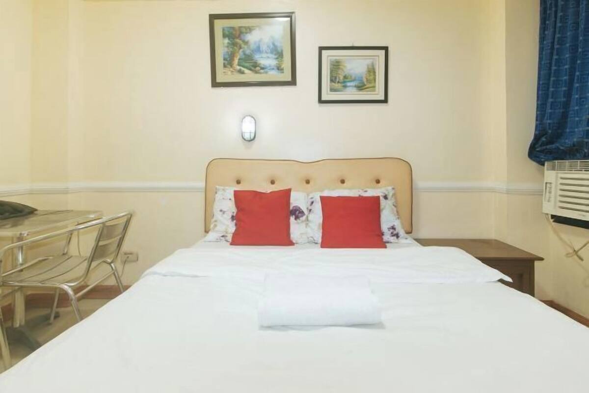 A hotel room with a bed, a small table, chairs, and two framed pictures on the wall.