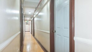 Un pasillo largo y estrecho con suelo de baldosas y puertas de madera a un lado.