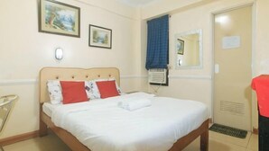 Una cama bien hecha con almohadas blancas y rojas, un cabecero de madera y un aire acondicionado de pared.
