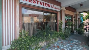 Fachada con un letrero que dice "WESTVIEW Pension" y un escaparate de vidrio con el texto "ABIERTO 24/7".