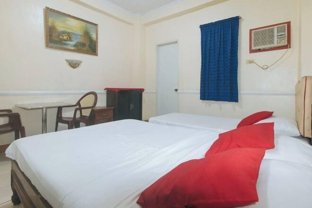 A hotel room with a bed, a desk, a chair, a wardrobe, and a painting on the wall.