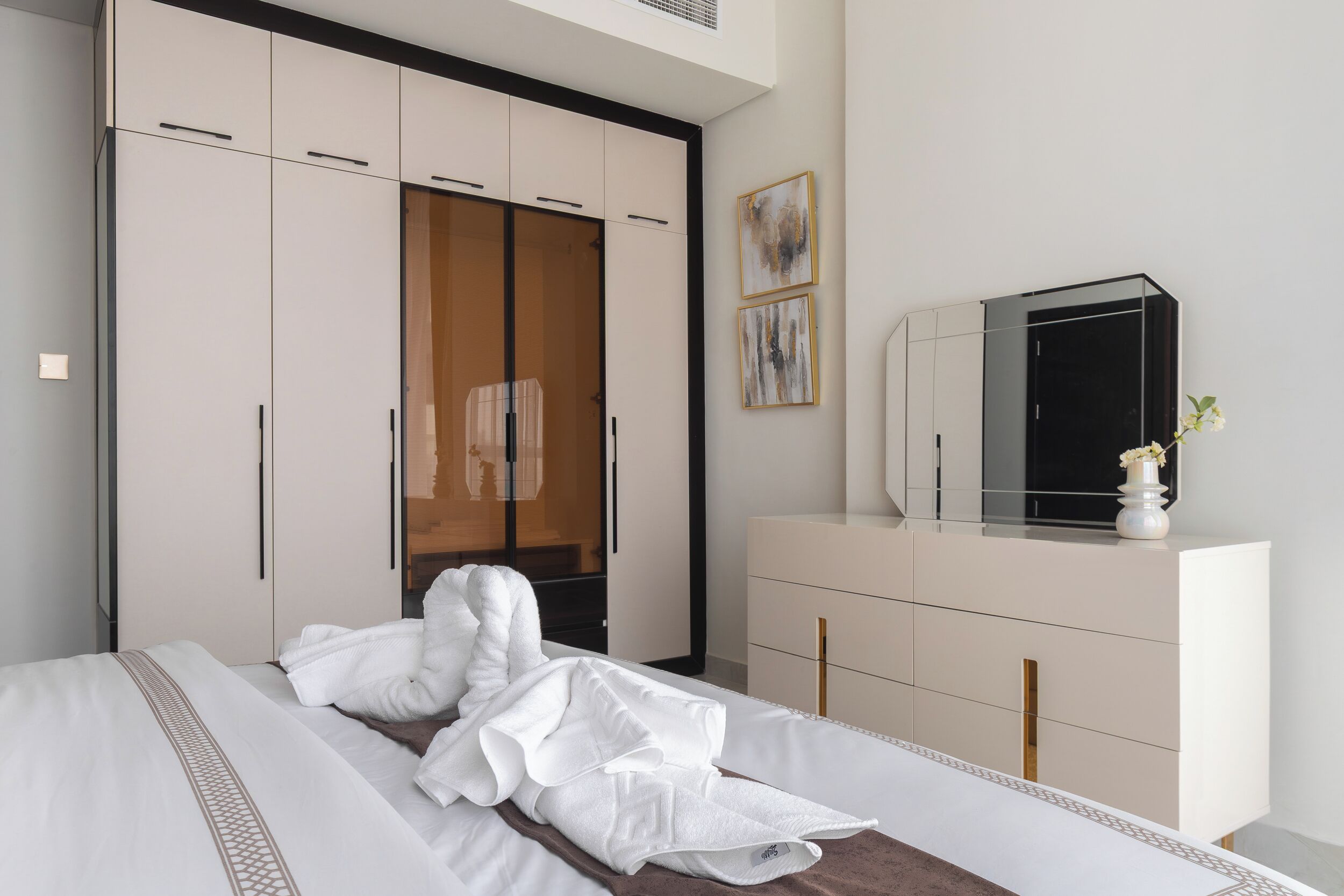 Une chambre d’hôtel comprenant un lit, une armoire, une coiffeuse avec un miroir et des œuvres d’art accrochées au mur.
