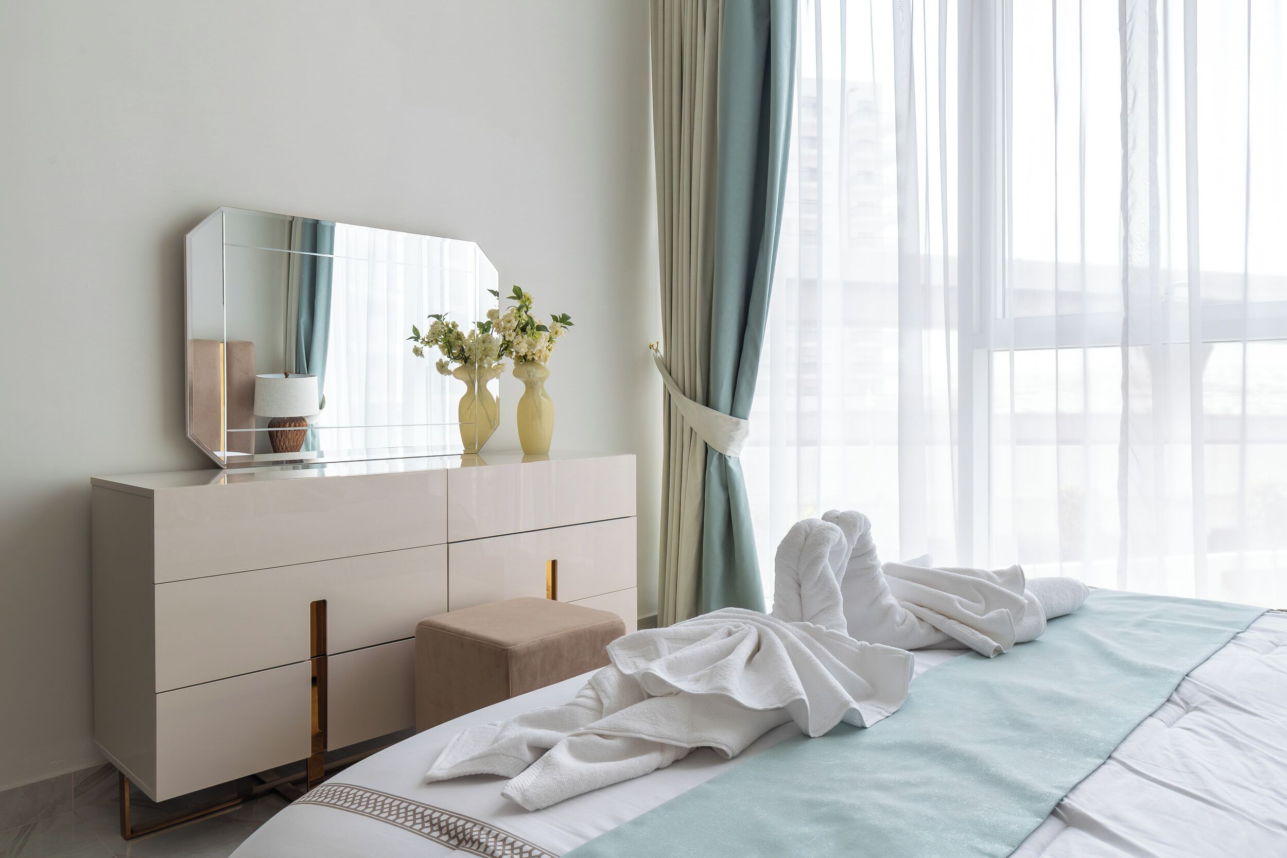 Ein Hotelzimmer mit Bett, Nachttisch mit Lampe, Spiegel und einem Fenster mit Vorhängen.