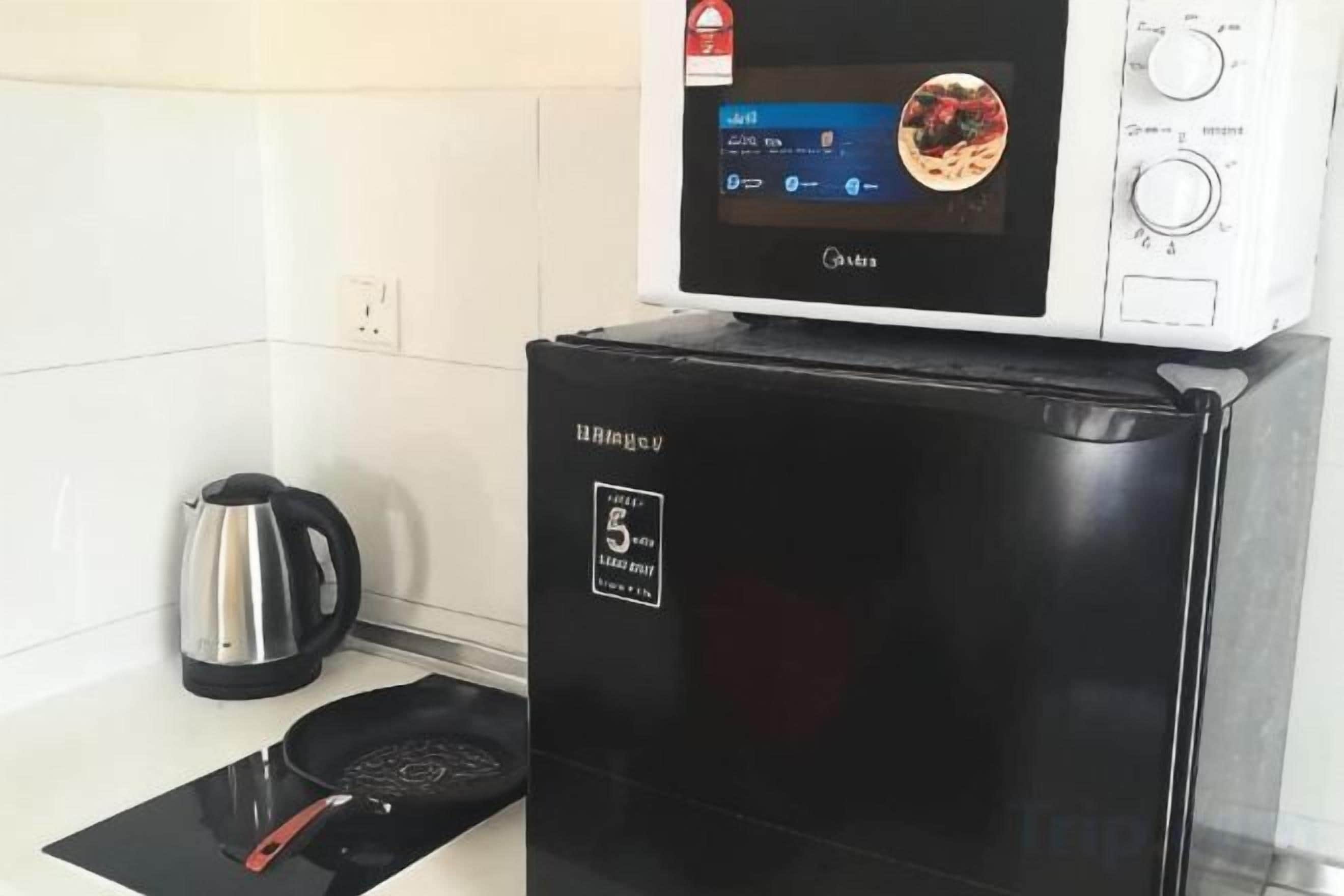 A compact kitchen with a microwave on top of a black refrigerator, a kettle, and a black induction cooktop.