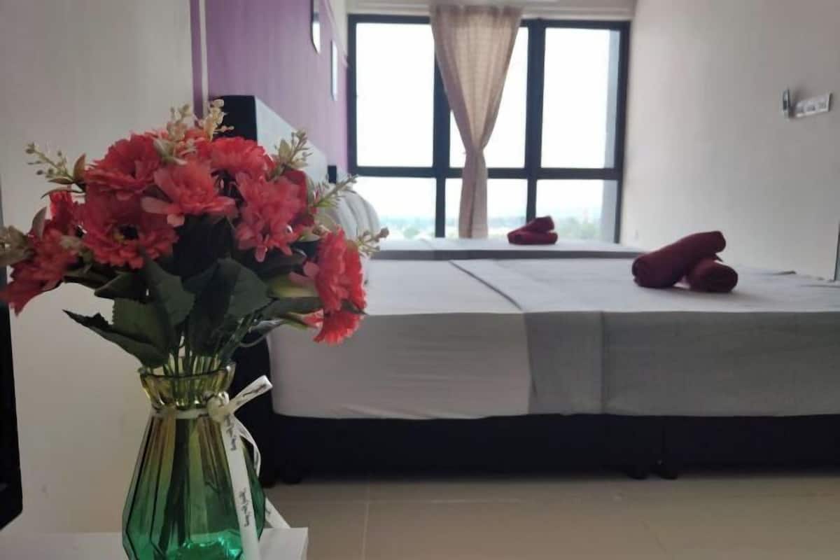 A hotel room with a bed, a window with curtains, and a vase with flowers on a table.